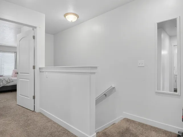 Upper-level landing featuring neutral carpeting, a white half-wall railing, and a functional overhead light fixture