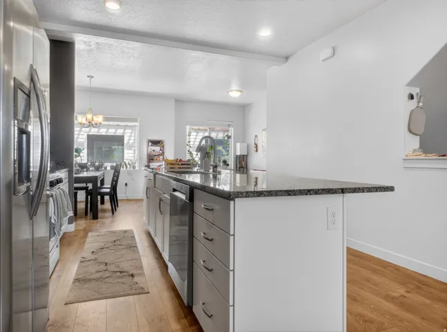 Spacious kitchen featuring a large island with a stone-finish countertop, stainless steel appliances, wood-finish flooring, recessed lighting, and white cabinetry
