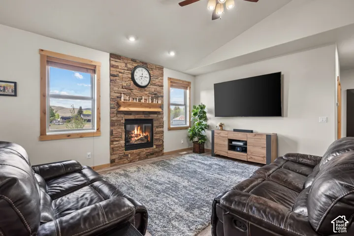 Living room featuring a stone-clad fireplace with a wood mantle, vaulted ceilings, recessed lighting, and wood-finish flooring