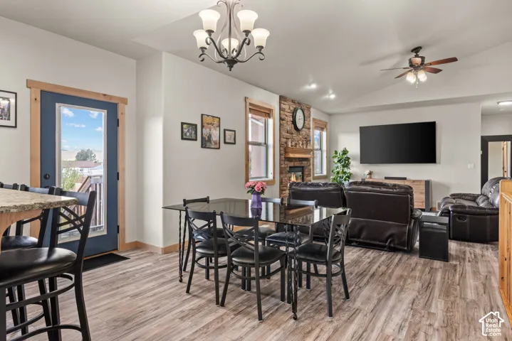 Open-concept living area featuring wood-finish flooring, a stone-faced fireplace, a vaulted ceiling, and recessed lighting