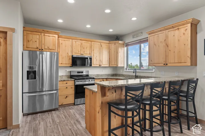 Kitchen featuring extensive light wood cabinetry, stainless steel appliances, granite countertops, wood-finish flooring, and recessed lighting