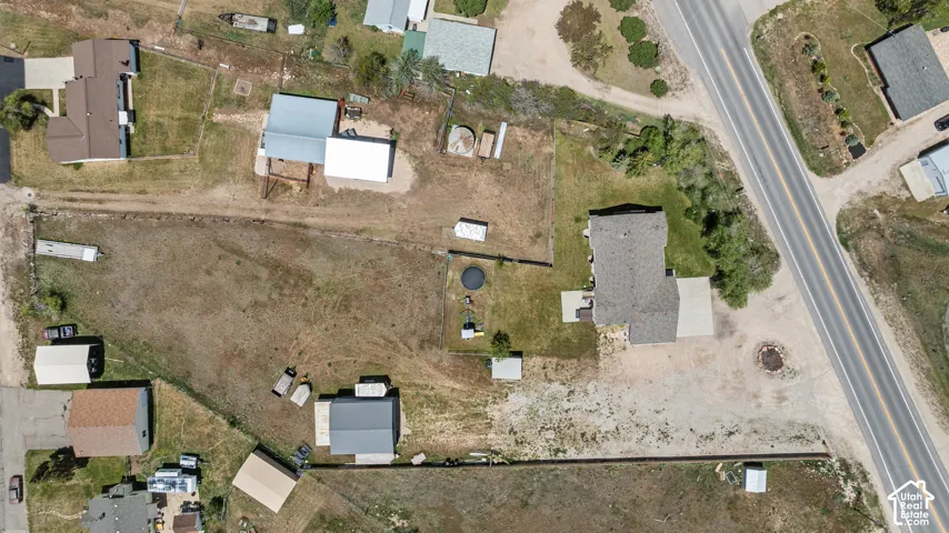 Expansive property featuring a main residence with a gray shingle roof, a secondary structure with a light gray roof, and a large open land area