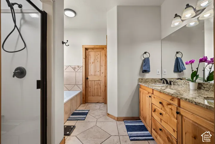 Bathroom featuring a wood-finish vanity with a light-colored countertop, a built-in shower with dark bronze hardware, a built-in bathtub with a tiled surround, a full-width mirror, and large format floor tiles
