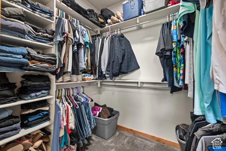 Walk-in closet featuring built-in shelving, multiple hanging rods, and wood-finish base trim
