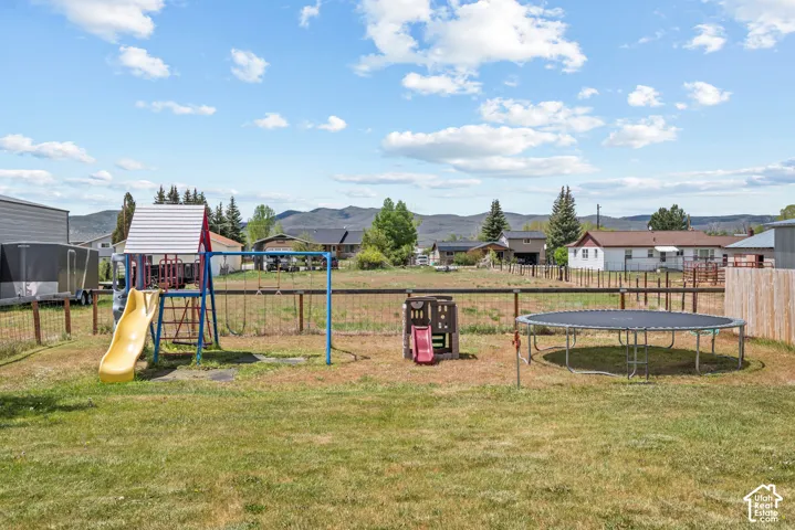 Expansive outdoor area featuring a full-size trampoline, a wooden playset with slide, and a swing set