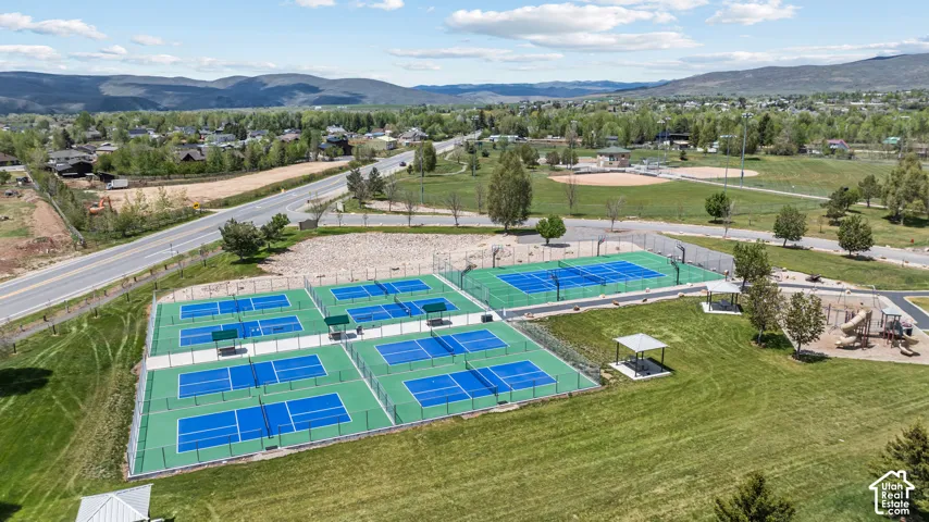 Expansive recreational area featuring multiple blue and green pickleball courts, tennis courts, a baseball field, and a dedicated playground area