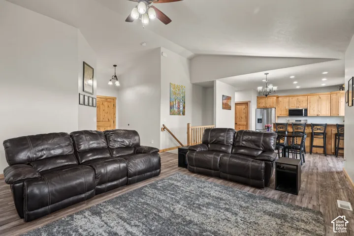 Open-concept living area featuring vaulted ceilings, wood-finish flooring, and a ceiling fan with integrated lighting