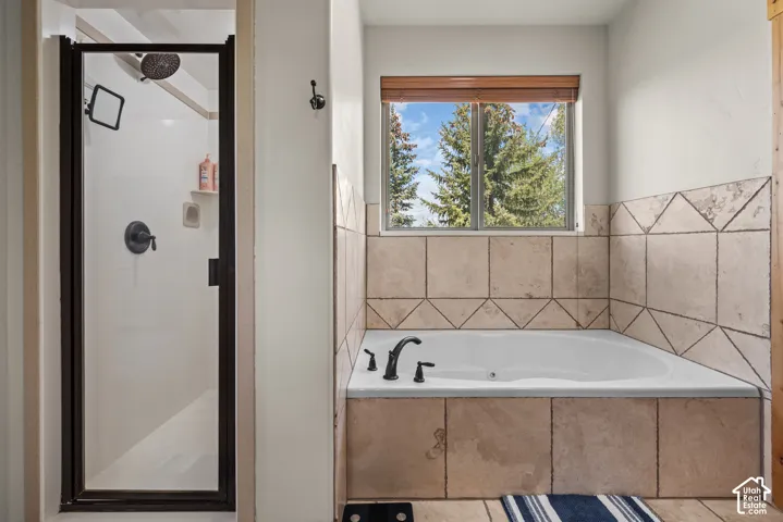Spacious bathroom featuring a corner soaking tub with tile surround, an adjacent shower with a dark-framed glass enclosure, and a window with natural light