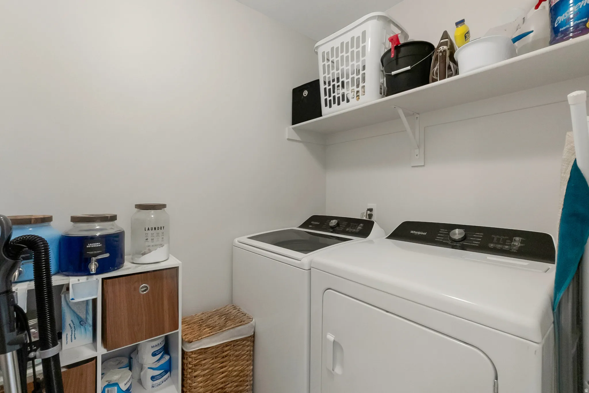 Dedicated laundry area featuring white walls, an upper storage shelf, and space for laundry appliances