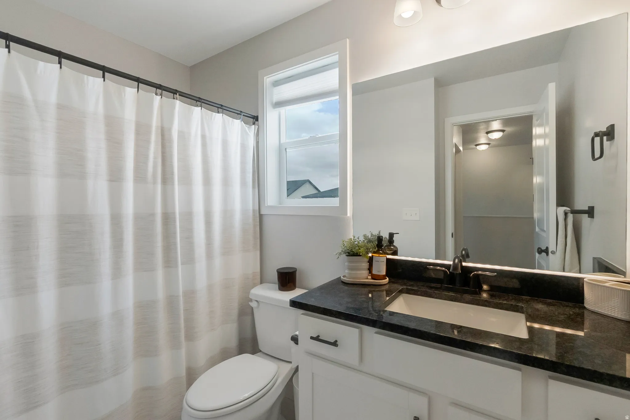 Bathroom featuring a single vanity with a dark countertop, an undermount sink, and matte black fixtures