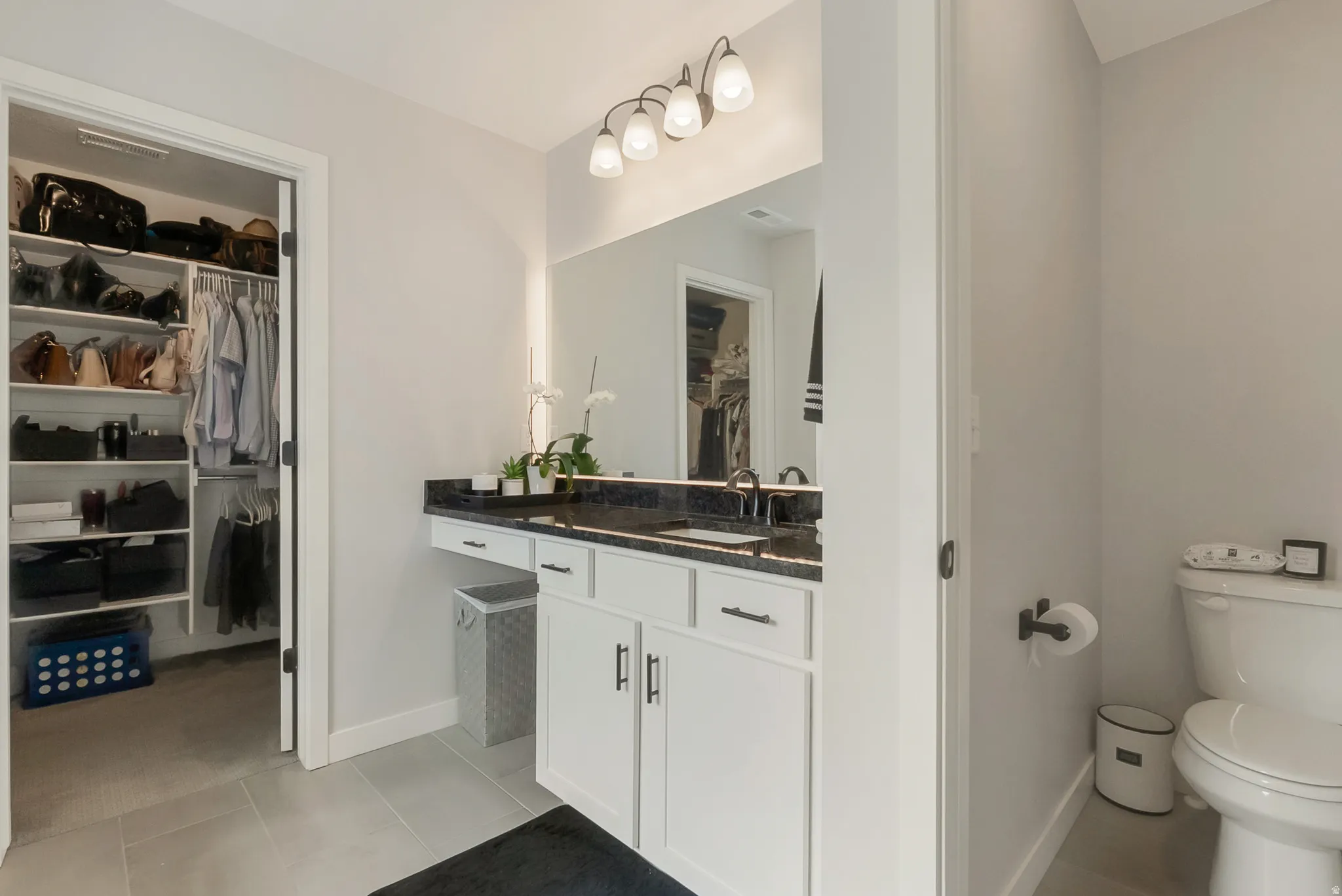 Bathroom featuring a dual-sink vanity with dark stone countertop, white cabinetry, and a framed mirror