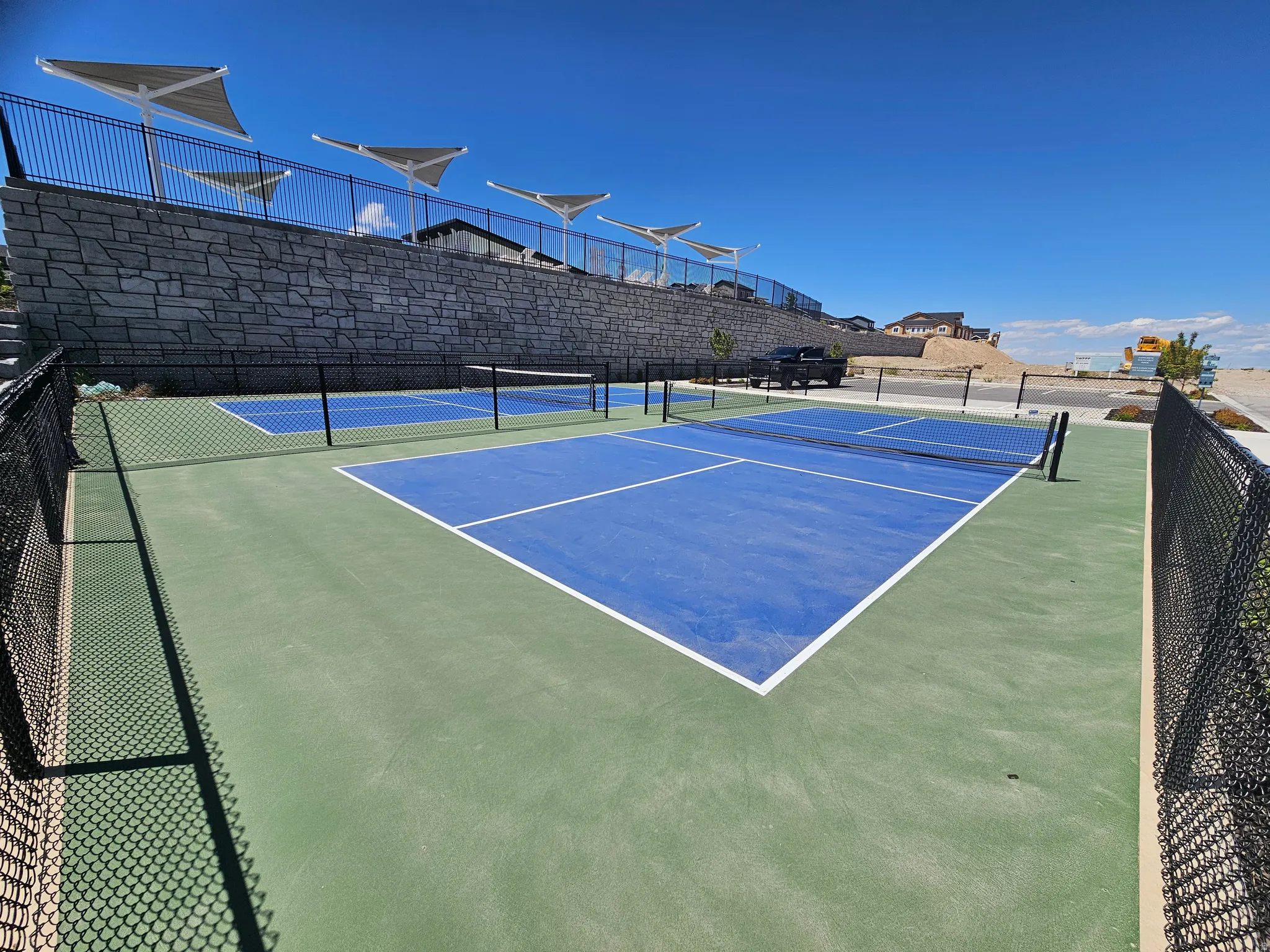 Two fenced pickleball courts featuring blue playing surfaces and green surrounds