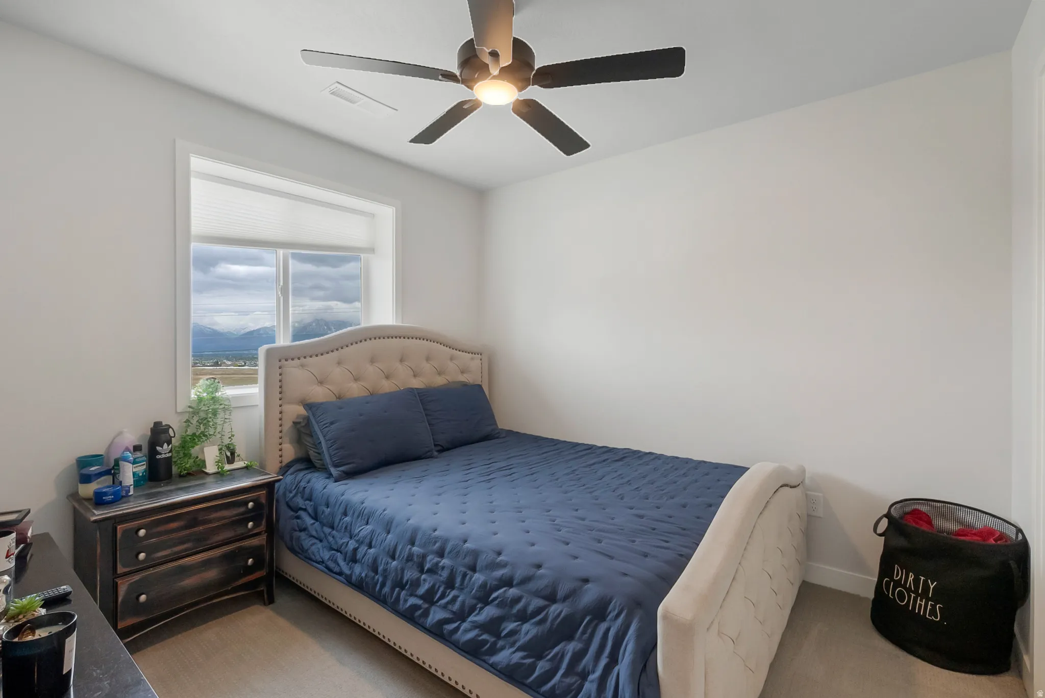 Bright bedroom featuring a large window, a remote-controlled ceiling fan, neutral wall paint, and beige carpet flooring