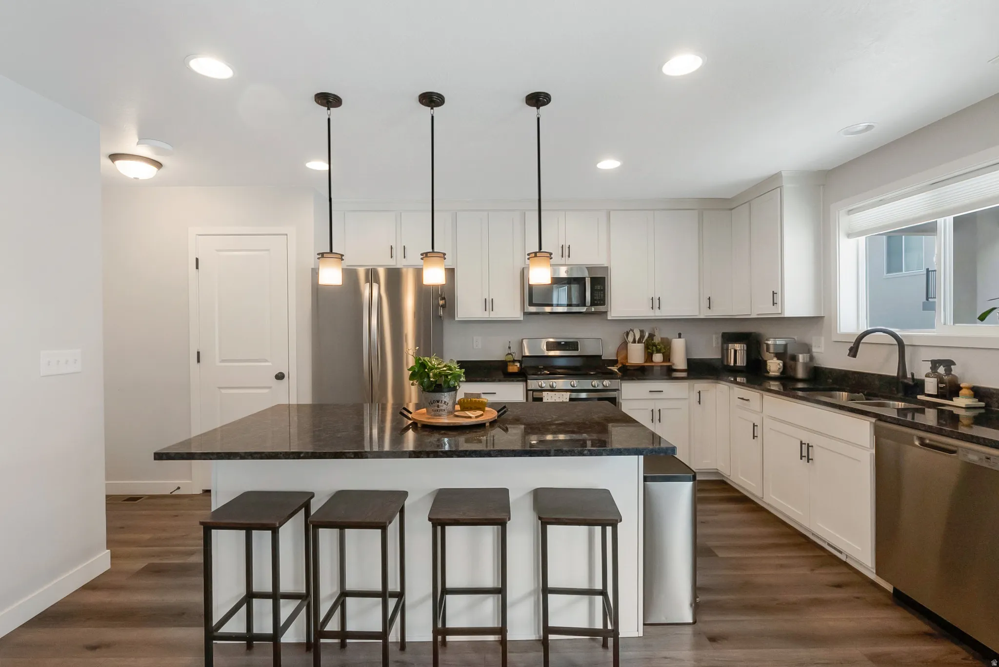 Kitchen featuring an island with pendant lighting, white cabinetry, dark countertops, and stainless steel appliances