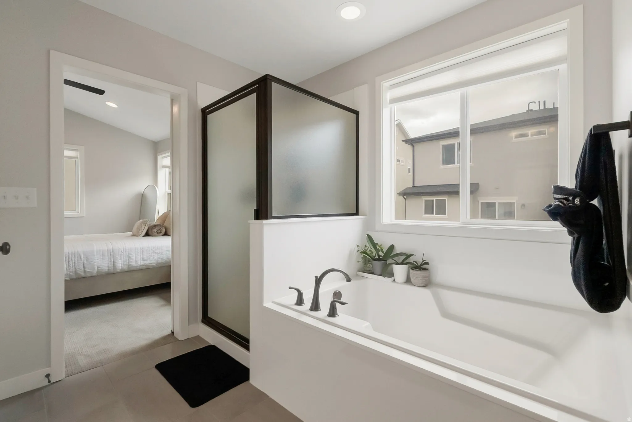 Bathroom featuring a built-in tub with a matte black faucet, a separate shower with frosted glass, and a large window providing natural light