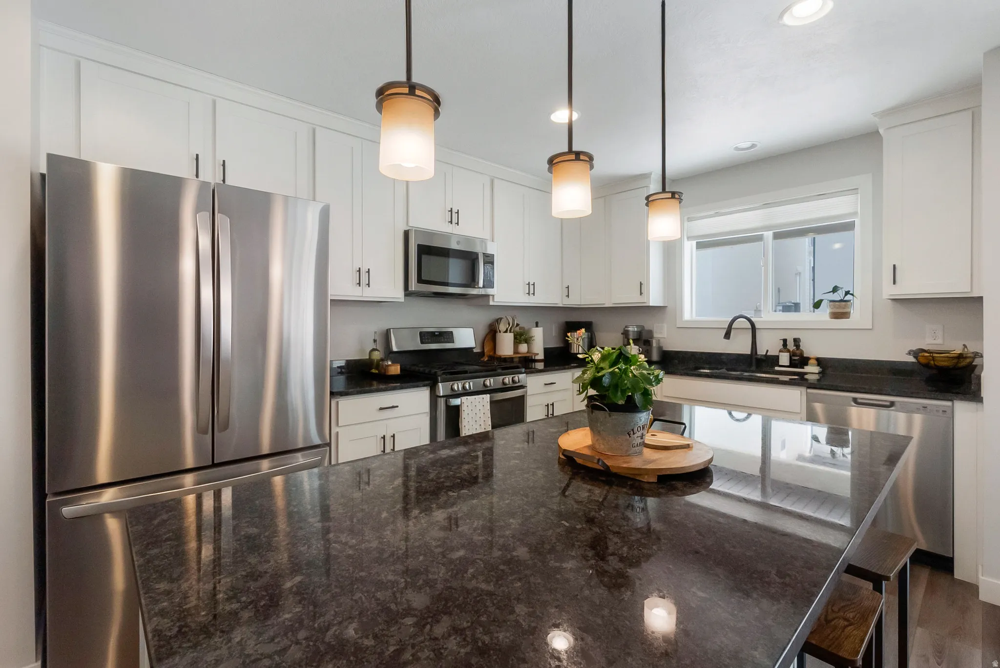 Contemporary kitchen featuring an expansive center island with dark stone countertops, white shaker cabinetry, stainless steel appliances, and pendant lighting