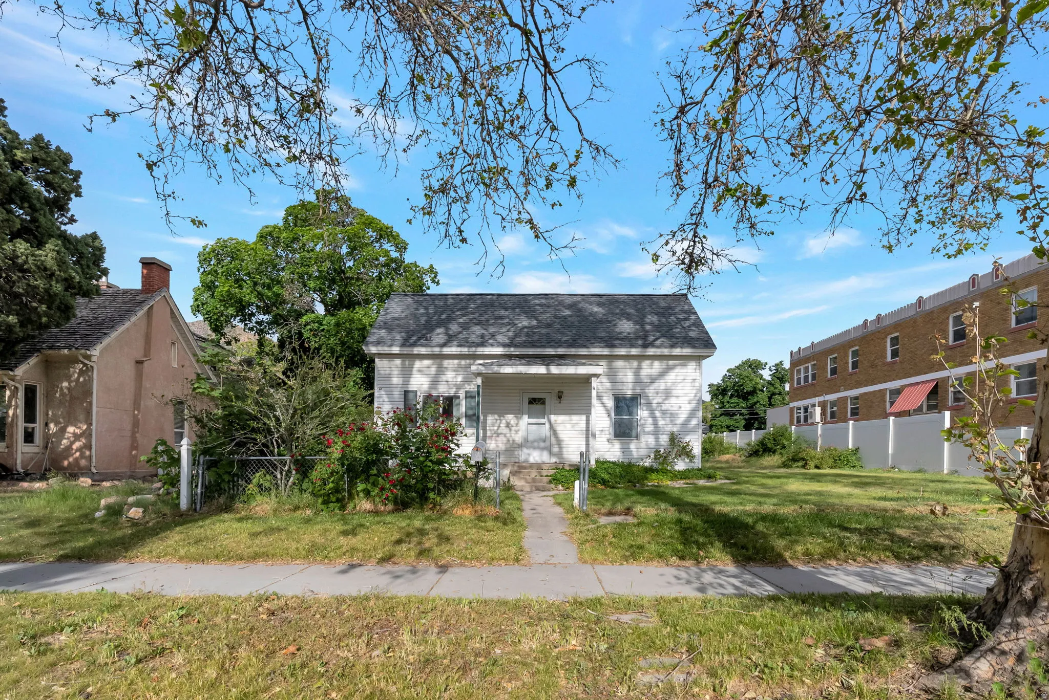 White exterior with a dark shingle roof and a concrete pathway leading to the entrance