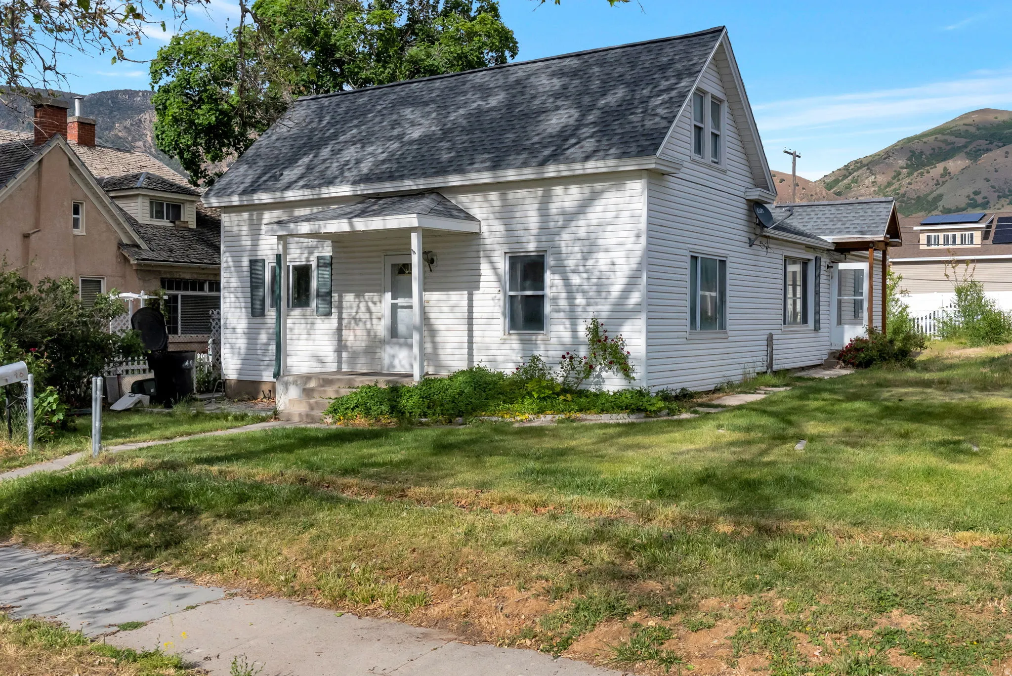 White siding exterior with a covered front porch, a dark shingle roof, and a partial mountain backdrop