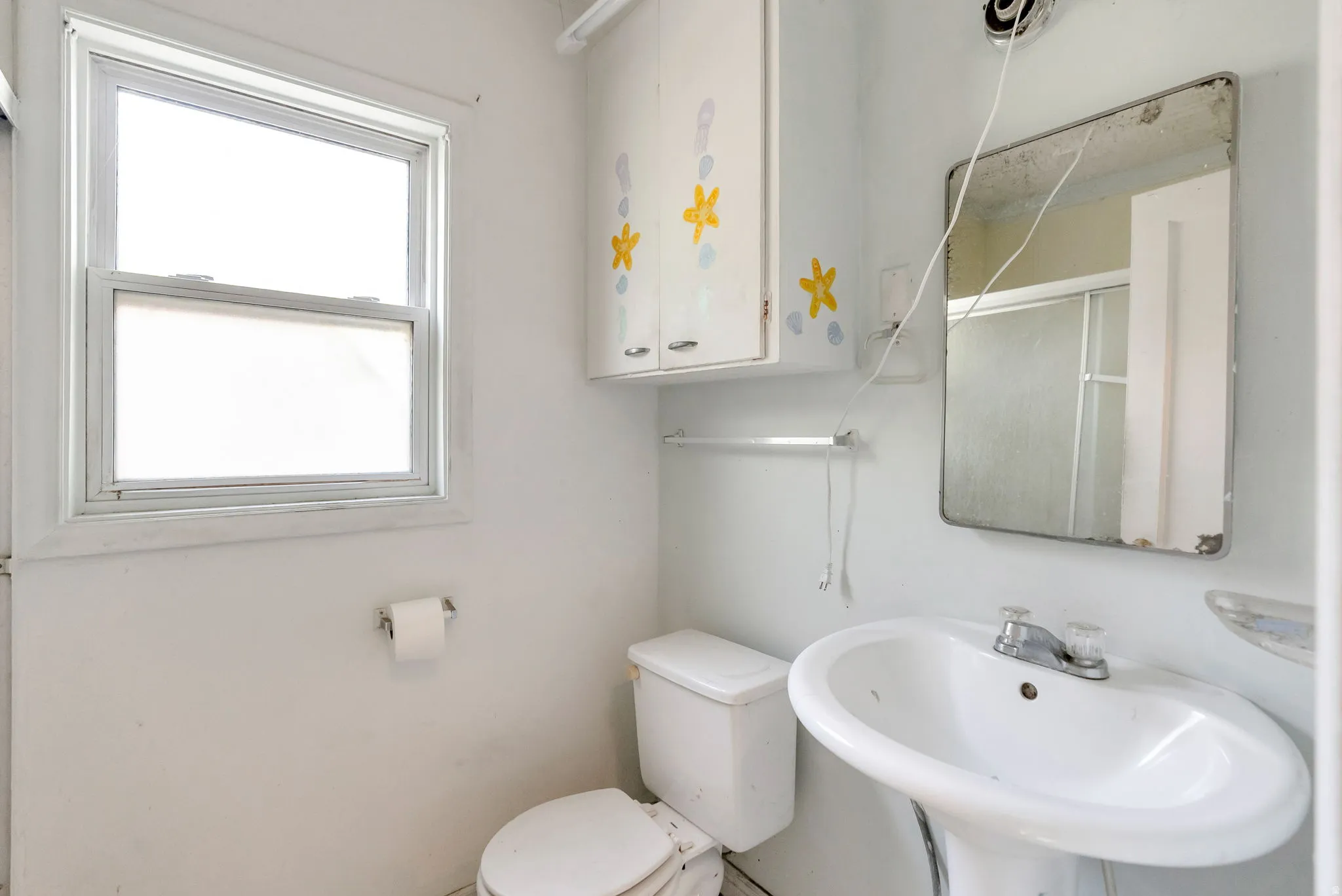 Pedestal sink with a two-handle faucet, wall-mounted mirror, and overhead cabinet storage