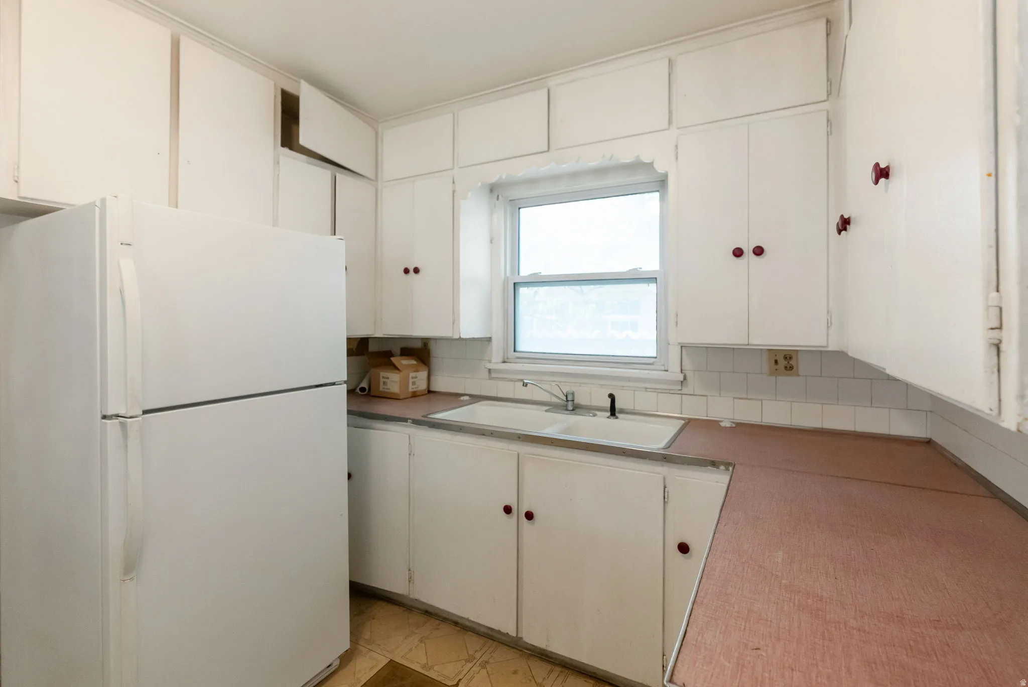Kitchen featuring white cabinetry with red hardware, a white double-basin sink with a black faucet, and a window above the sink
