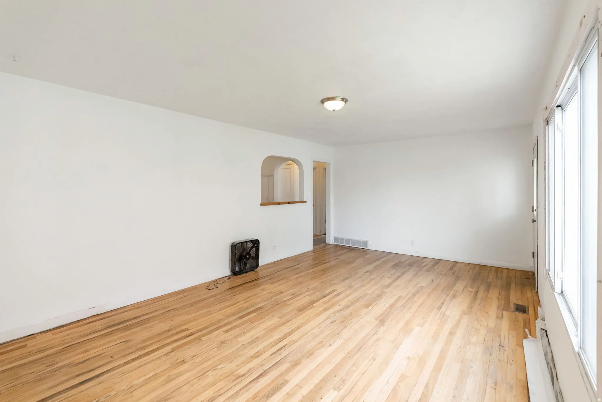 Hardwood flooring throughout the room, expansive windows providing abundant natural light, a built-in arched alcove with a wood sill, and a flush-mount ceiling light fixture
