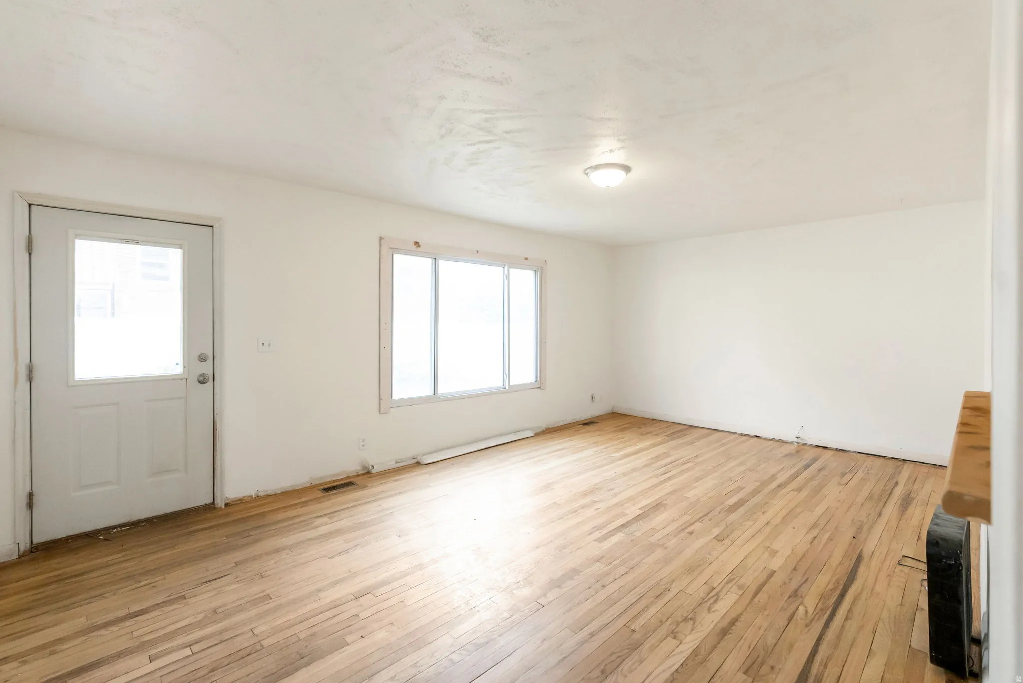 Spacious room featuring wood-finish flooring, white walls, and a multi-pane window