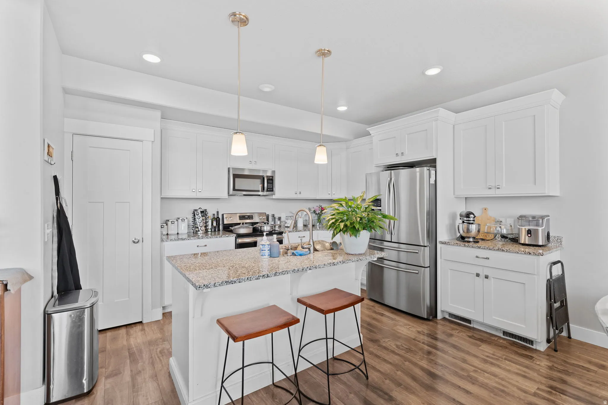Kitchen featuring white cabinetry with crown molding, stainless steel appliances, granite countertops, an island with pendant lighting, and wood-finish flooring