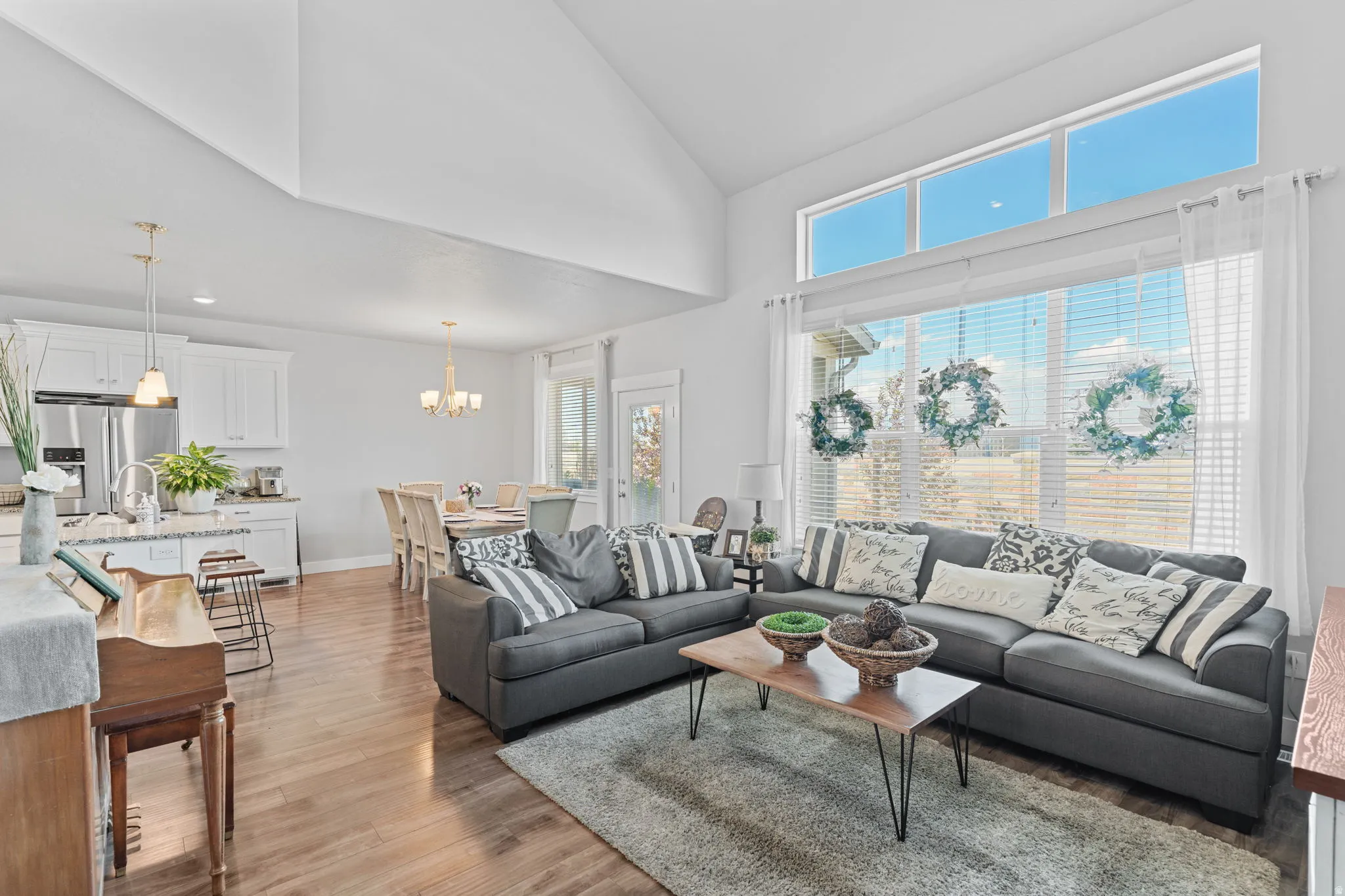 Expansive living area featuring vaulted ceilings, wood-finish flooring, and a large window wall with upper transom windows