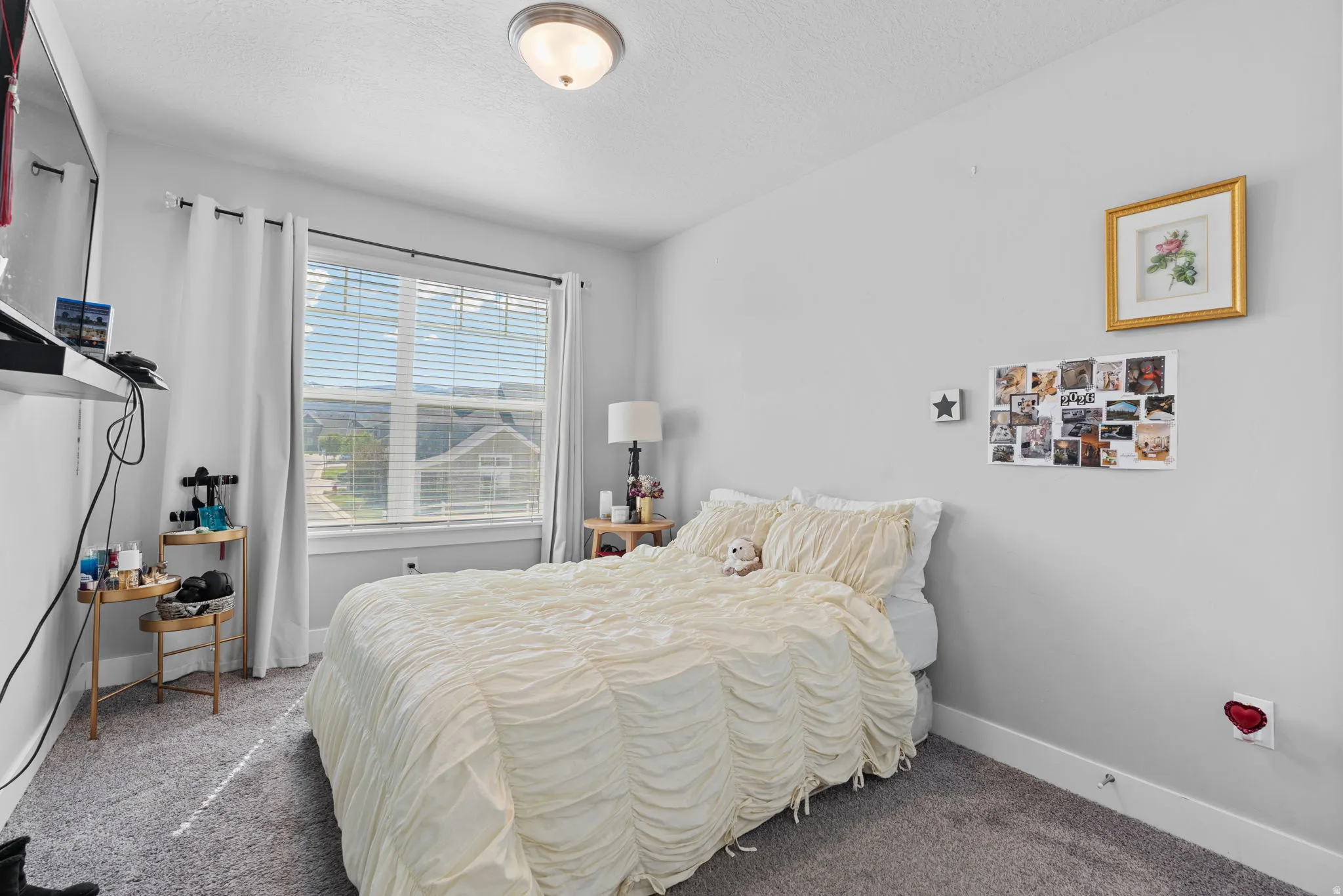 Bedroom featuring a large window with white blinds, neutral wall paint, and gray carpet flooring