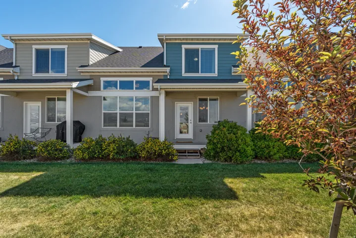 Rear elevation featuring varied siding, multiple window designs, a ground-level patio, and surrounding green space with established shrubbery