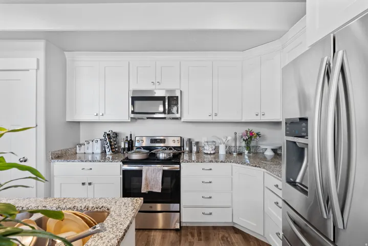 Contemporary kitchen featuring white shaker cabinetry, stainless steel appliances, speckled stone countertops, and wood-finish flooring