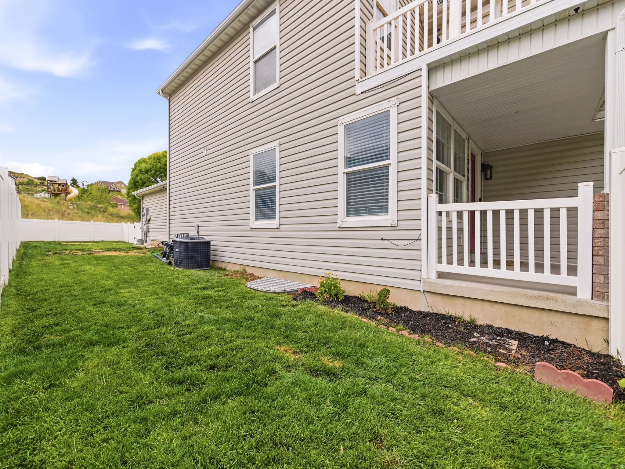 Side yard with expansive green lawn with a white privacy fence