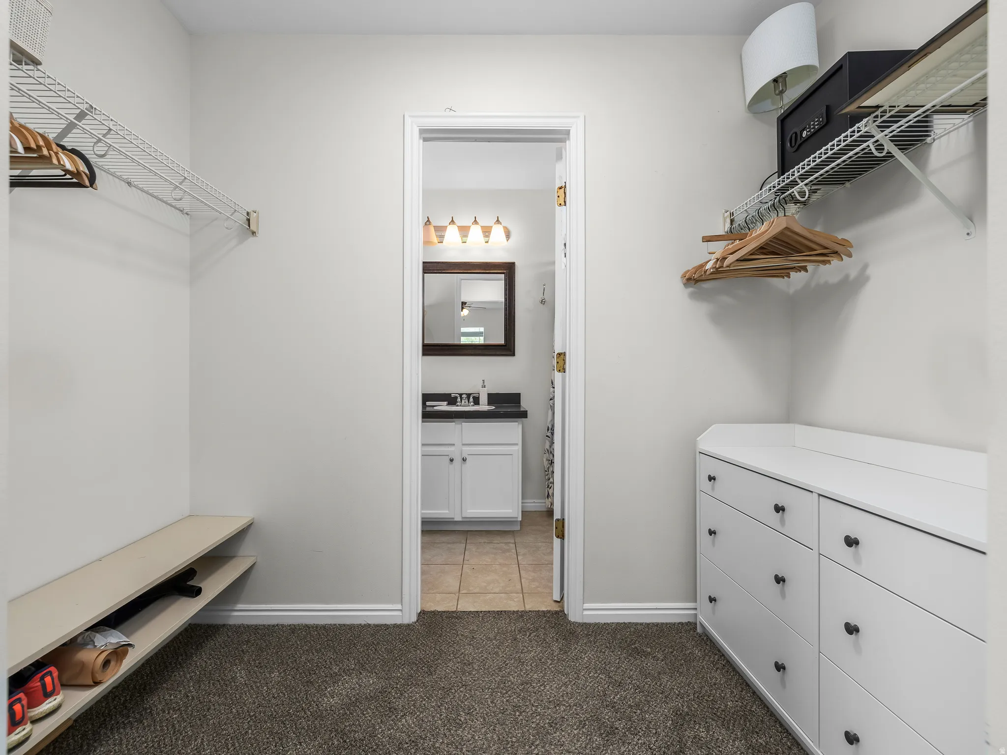 Master walk-in closet featuring built-in shelving, white wire racks, and a white dresser included with dark hardware