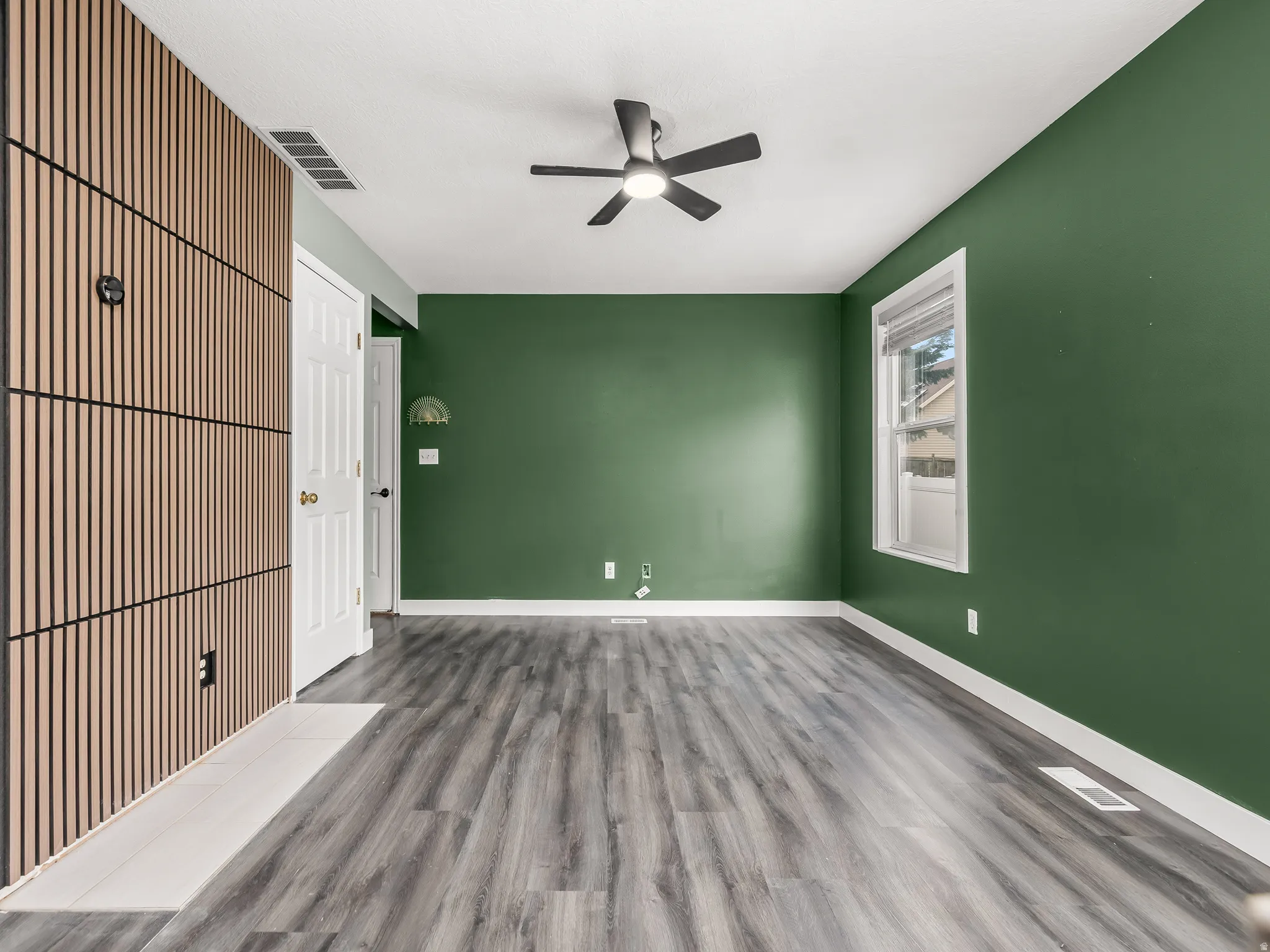 Room with wood-finish flooring, a contemporary ceiling fan, and a window with white trim