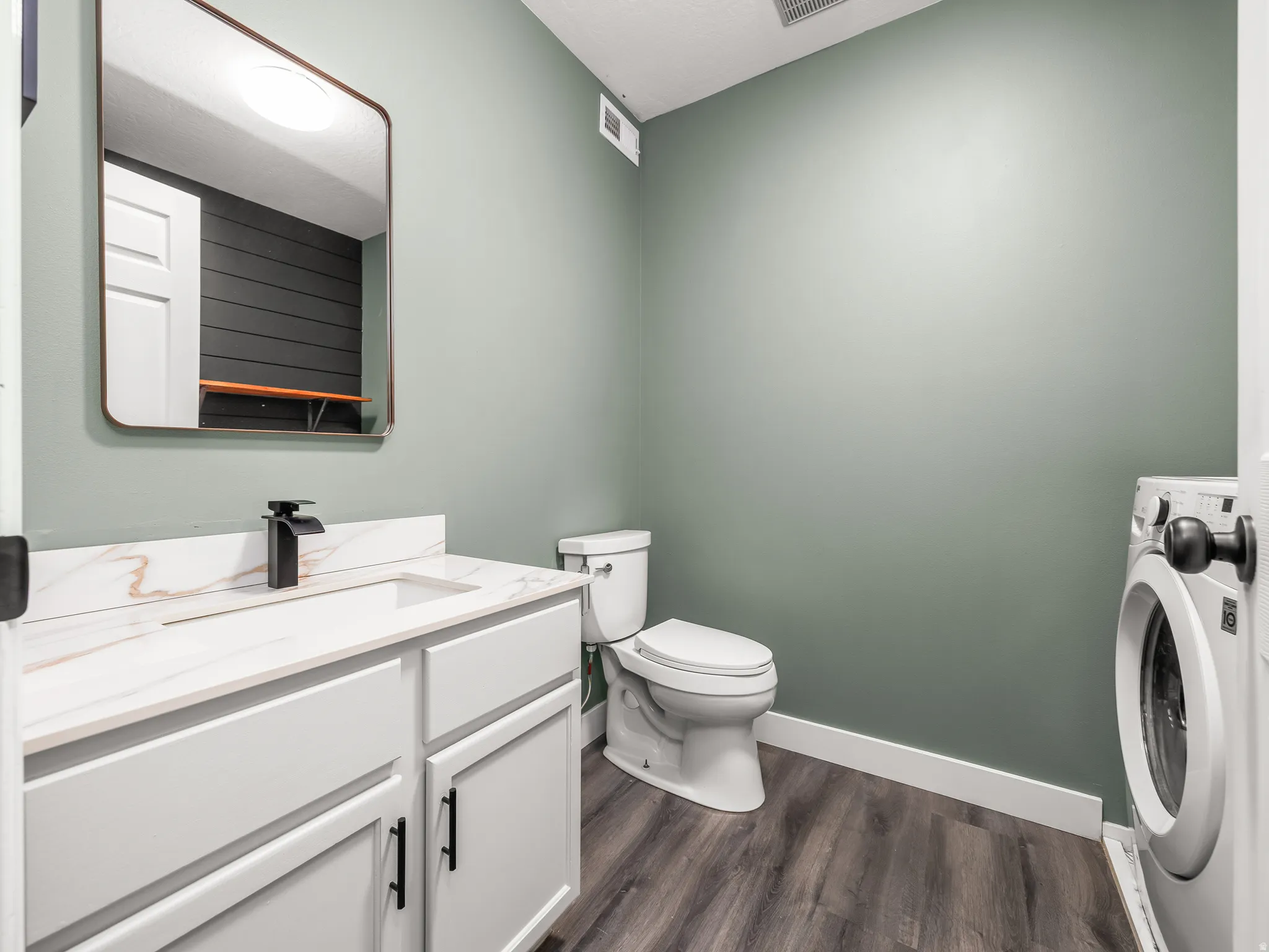 Bathroom/laundry Contemporary vanity with a white countertop and integrated sink, matte black faucet, and rectangular mirror. Washer and dryer are included.
