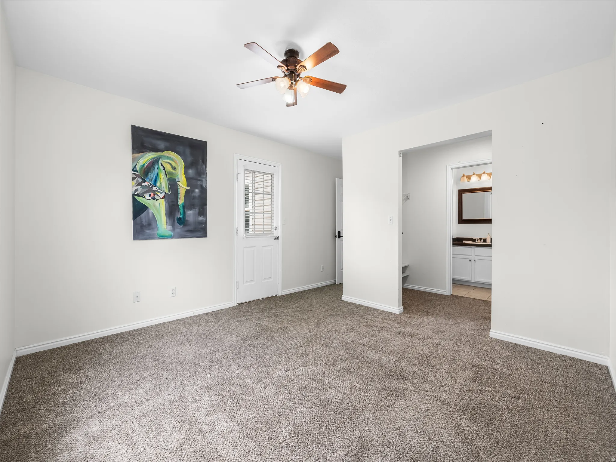 Master bedroom into the closet. Carpeted room featuring a ceiling fan, white baseboards, and a paneled door with louvered glass