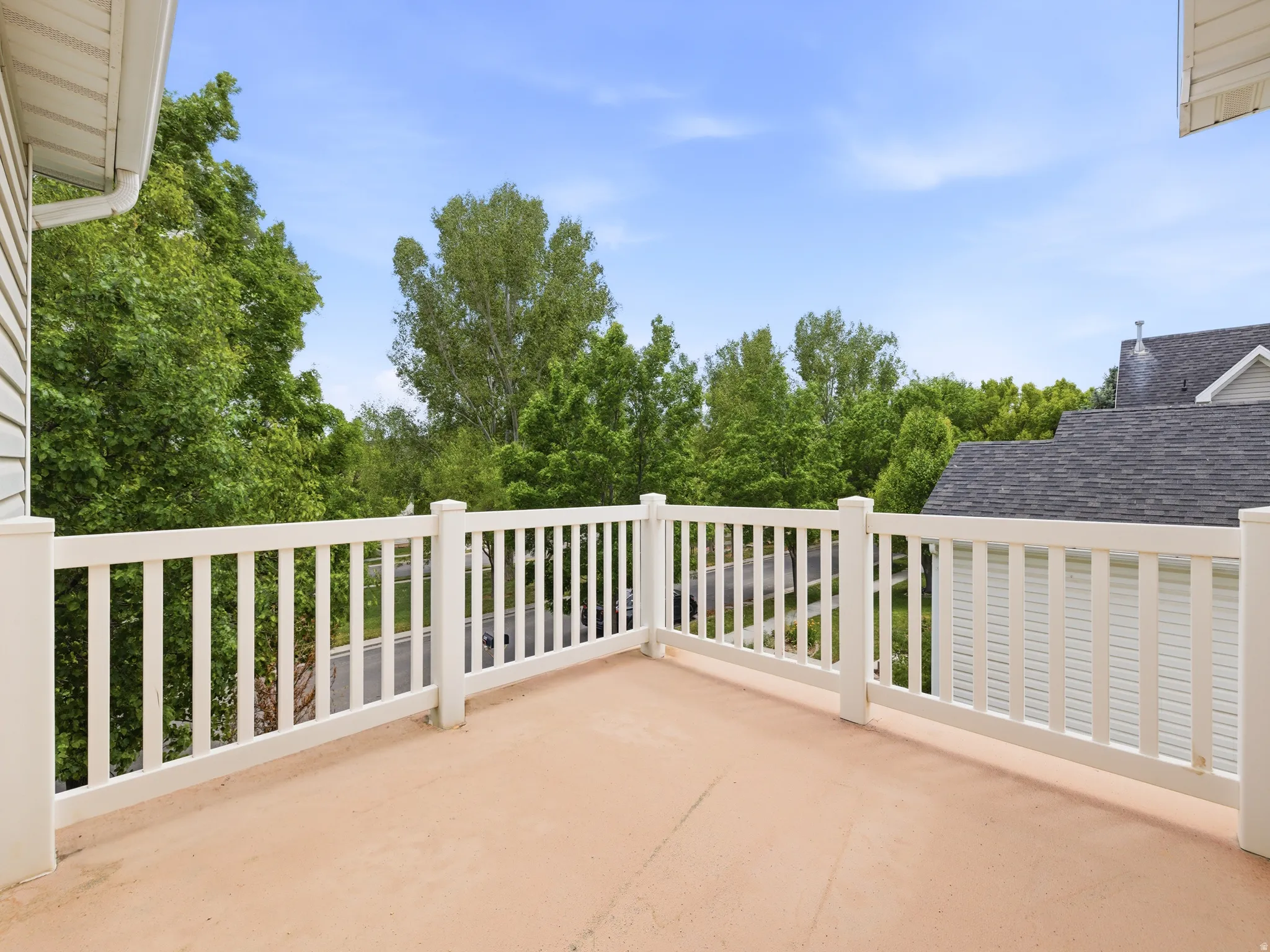 Outdoor deck off the master featuring a beige surface and white railings, surrounded by mature green trees