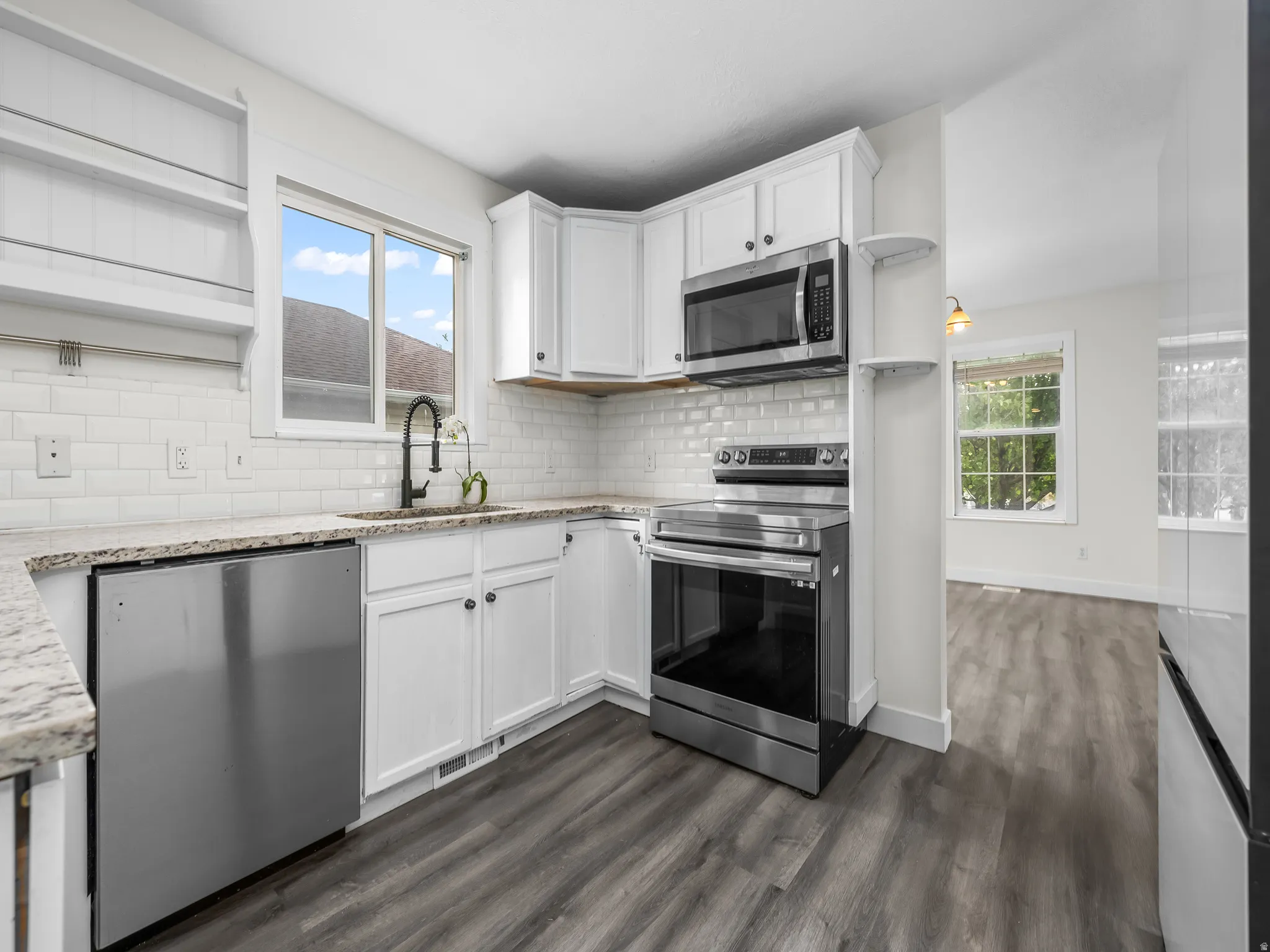 Contemporary kitchen featuring white cabinetry, stainless steel appliances, a subway tile backsplash, and wood-finish flooring
