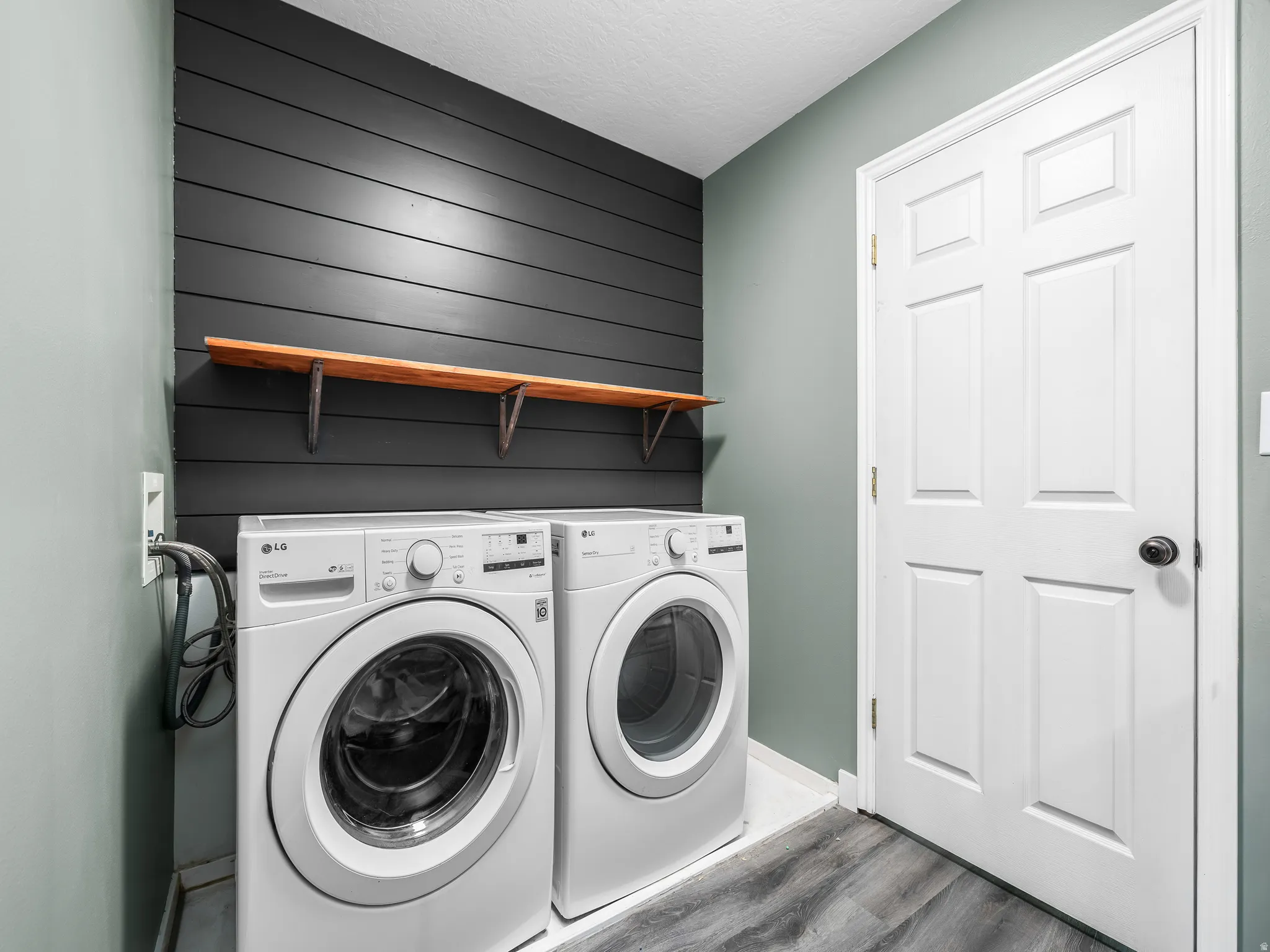Laundry area/bathroom featuring a dark shiplap accent wall, light wood-finish shelving, and wood-look flooring. Washer and dryer are included.