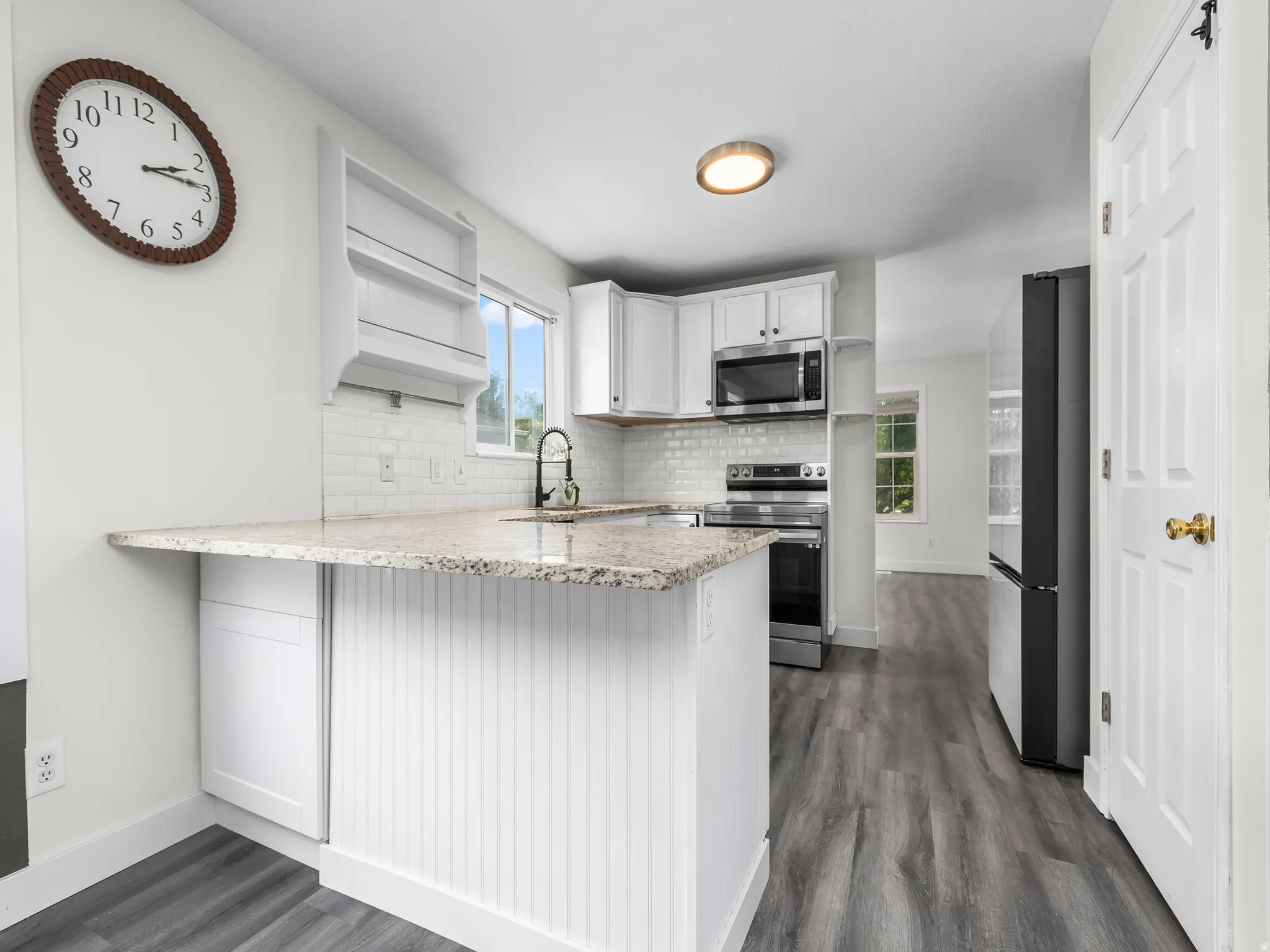 Bright kitchen featuring granite countertops, white subway tile backsplash, white cabinetry, stainless steel appliances, and wood-finish flooring. Fridge is included.