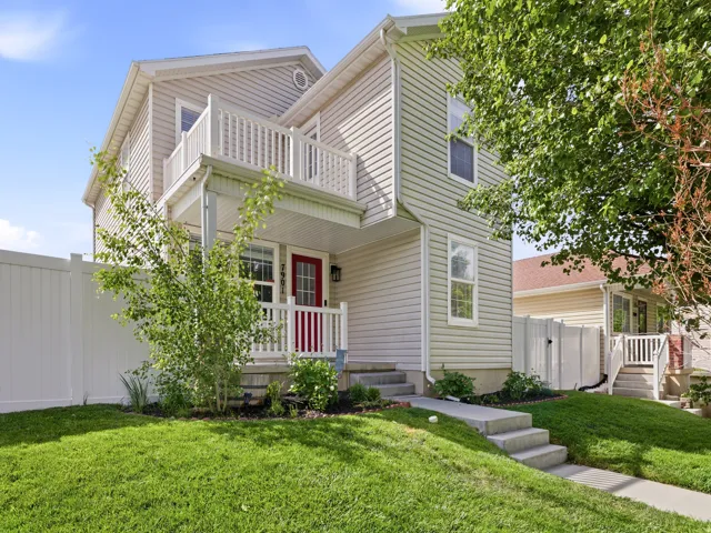 Two-story residence featuring light-toned siding, a vibrant red front door, and a second-level balcony with white railings