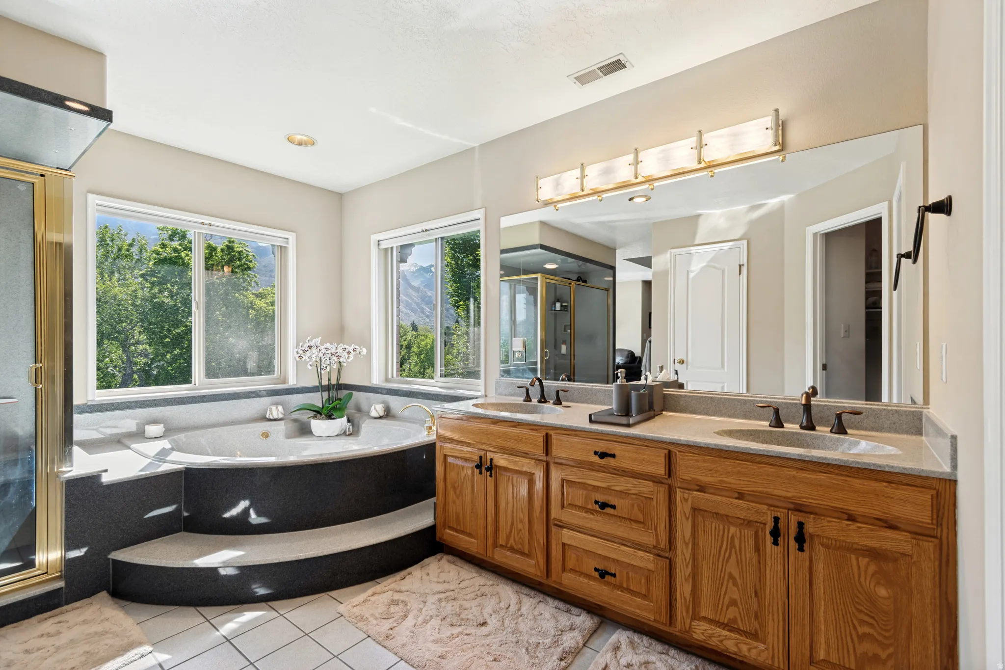 Bathroom featuring a corner soaking tub with built-in steps, dual vanity with wood cabinetry, and a mirrored wall