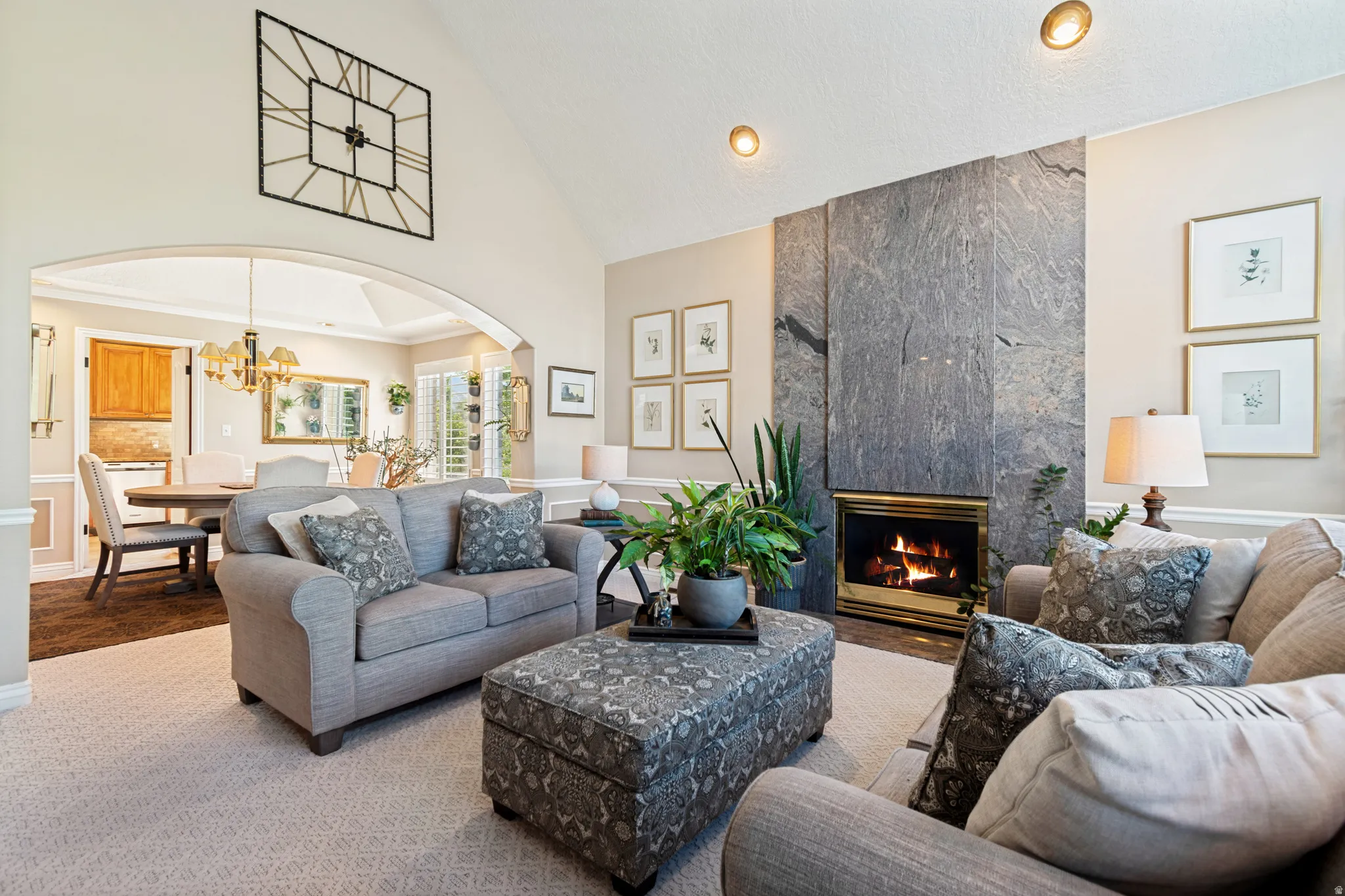 Spacious living area featuring a stone-clad fireplace with a brass firebox, vaulted ceilings, recessed lighting, and an arched entry to the dining room