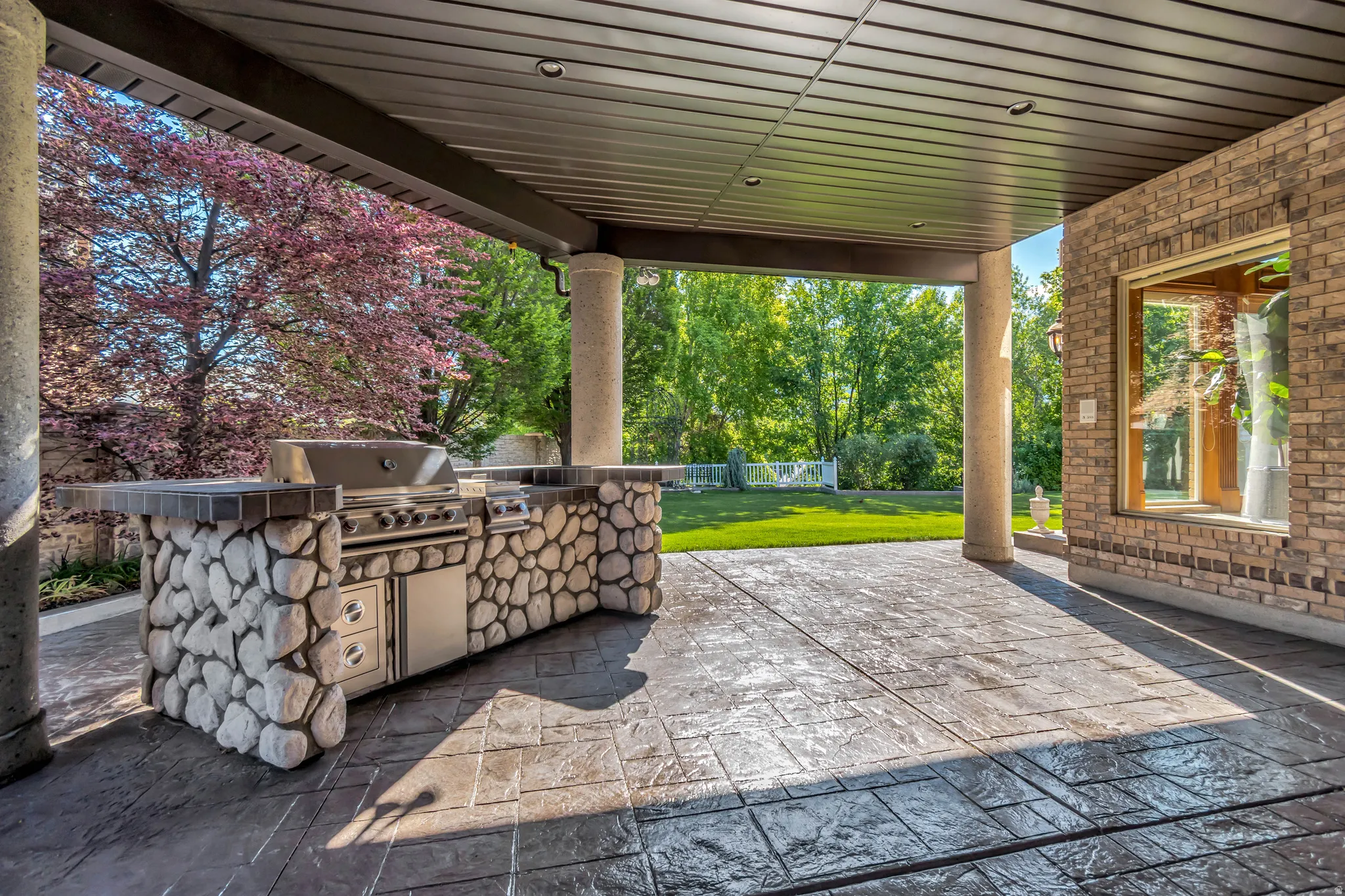 Covered patio featuring an outdoor kitchen with integrated grill, stone-clad base, and stamped concrete flooring