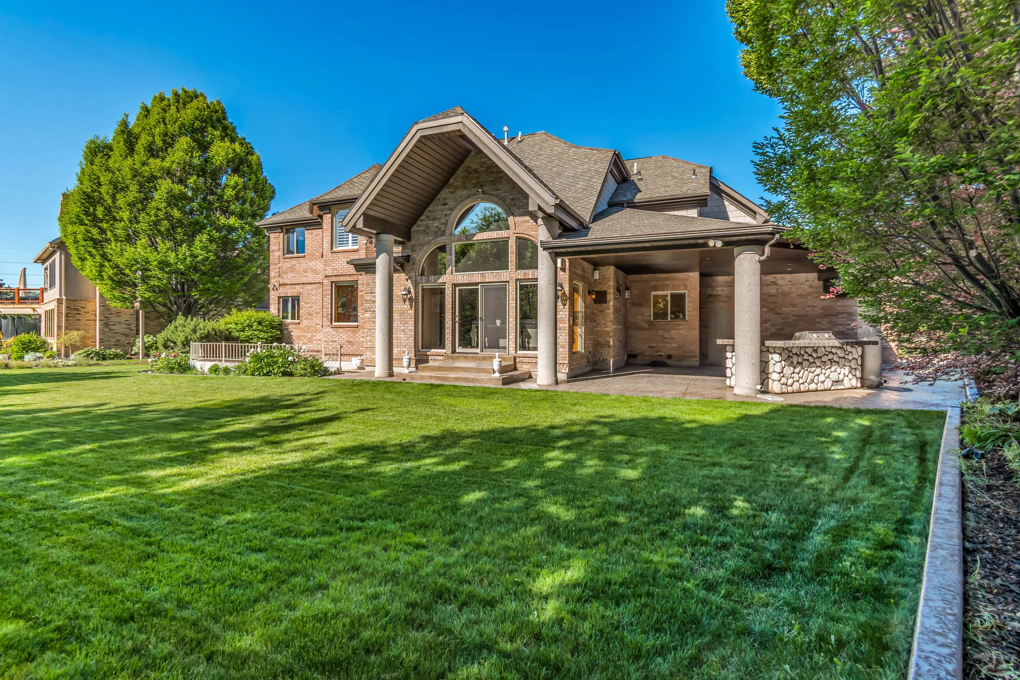 Expansive lawn area featuring a multi-level brick exterior and a covered patio