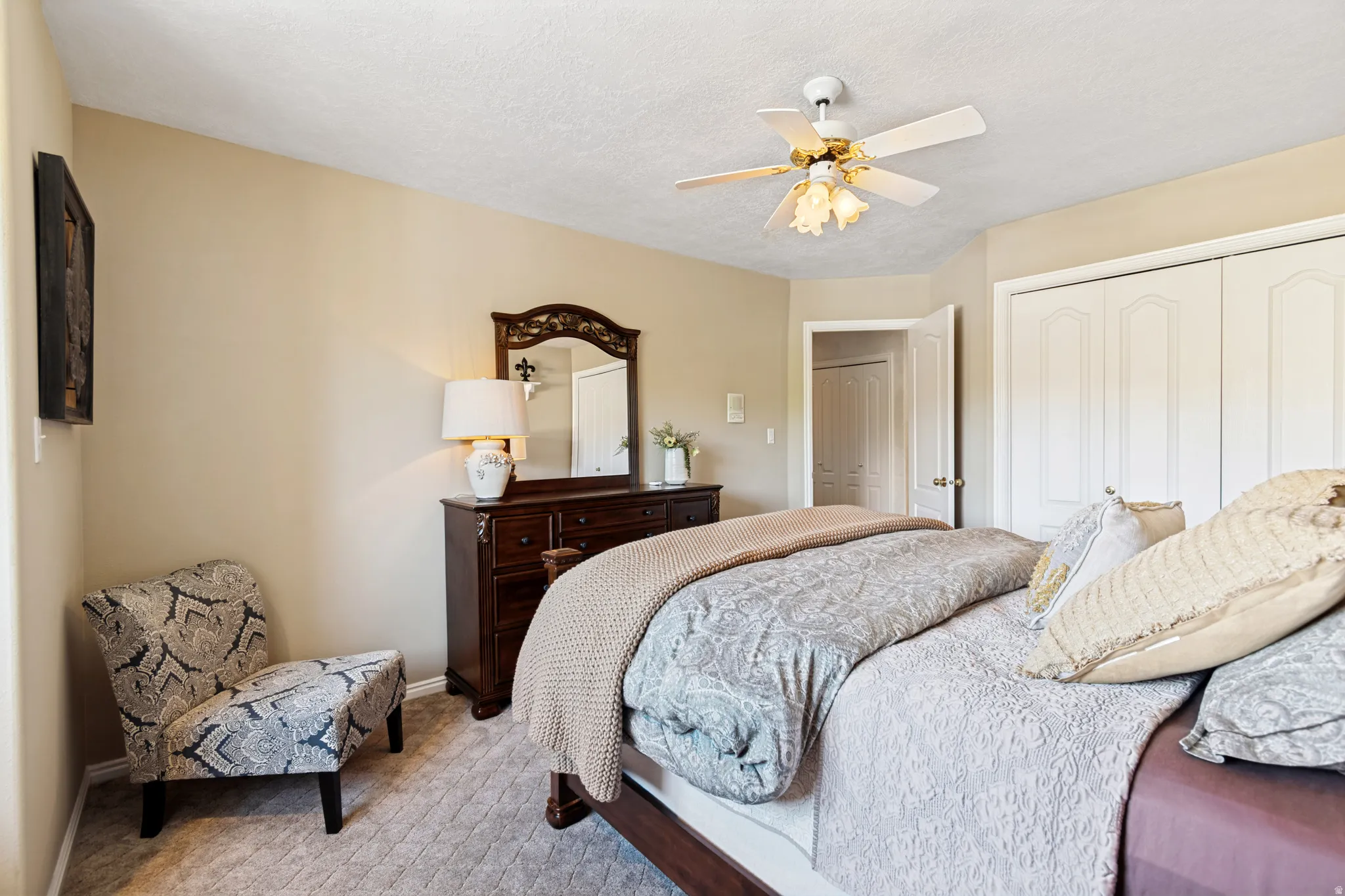 Carpeted room featuring a ceiling fan, light-toned walls, louvered closet doors, and an additional doorway