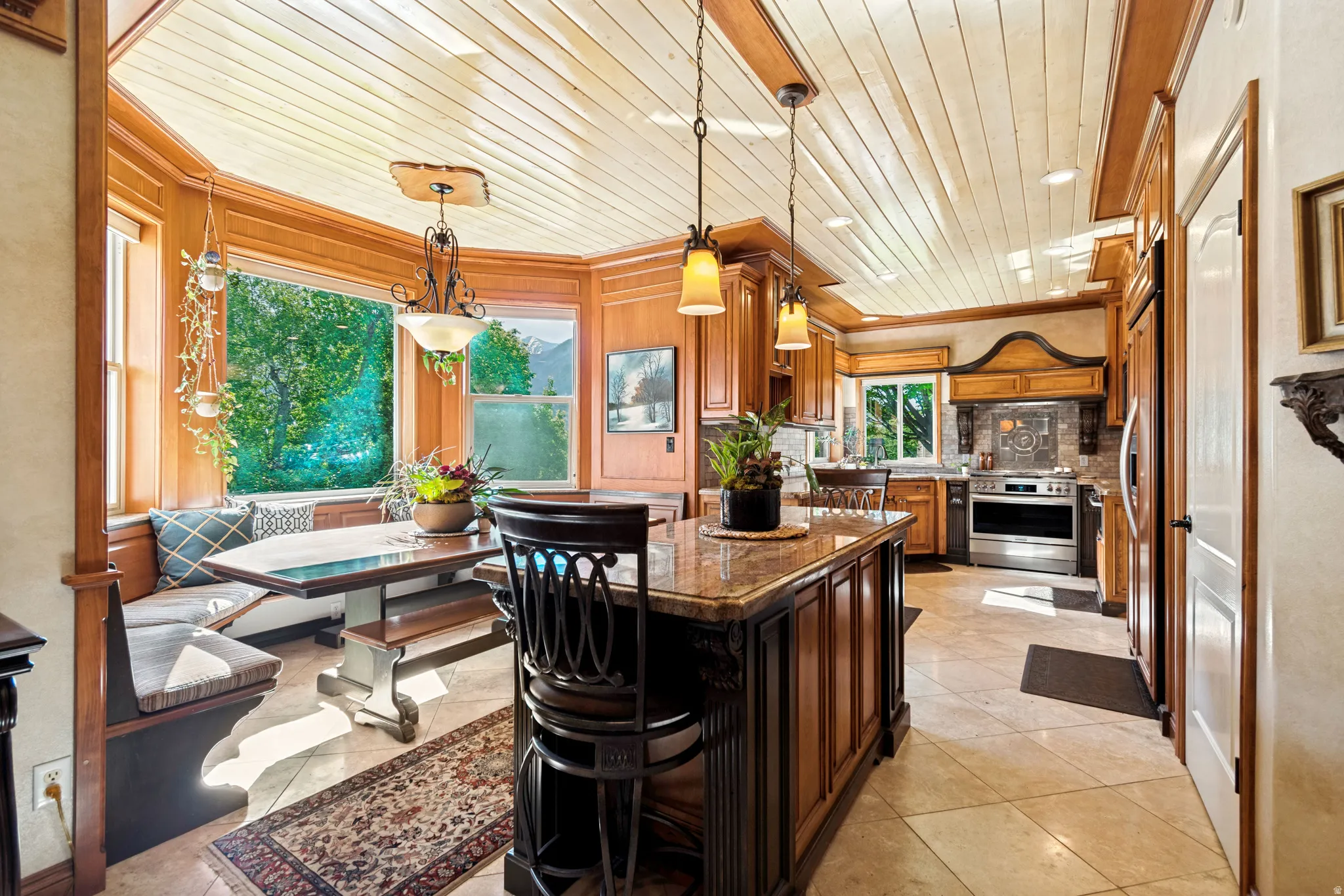 Kitchen featuring a built-in banquette, central island with pendant lighting, wood cabinetry, tile flooring, and stainless steel appliances