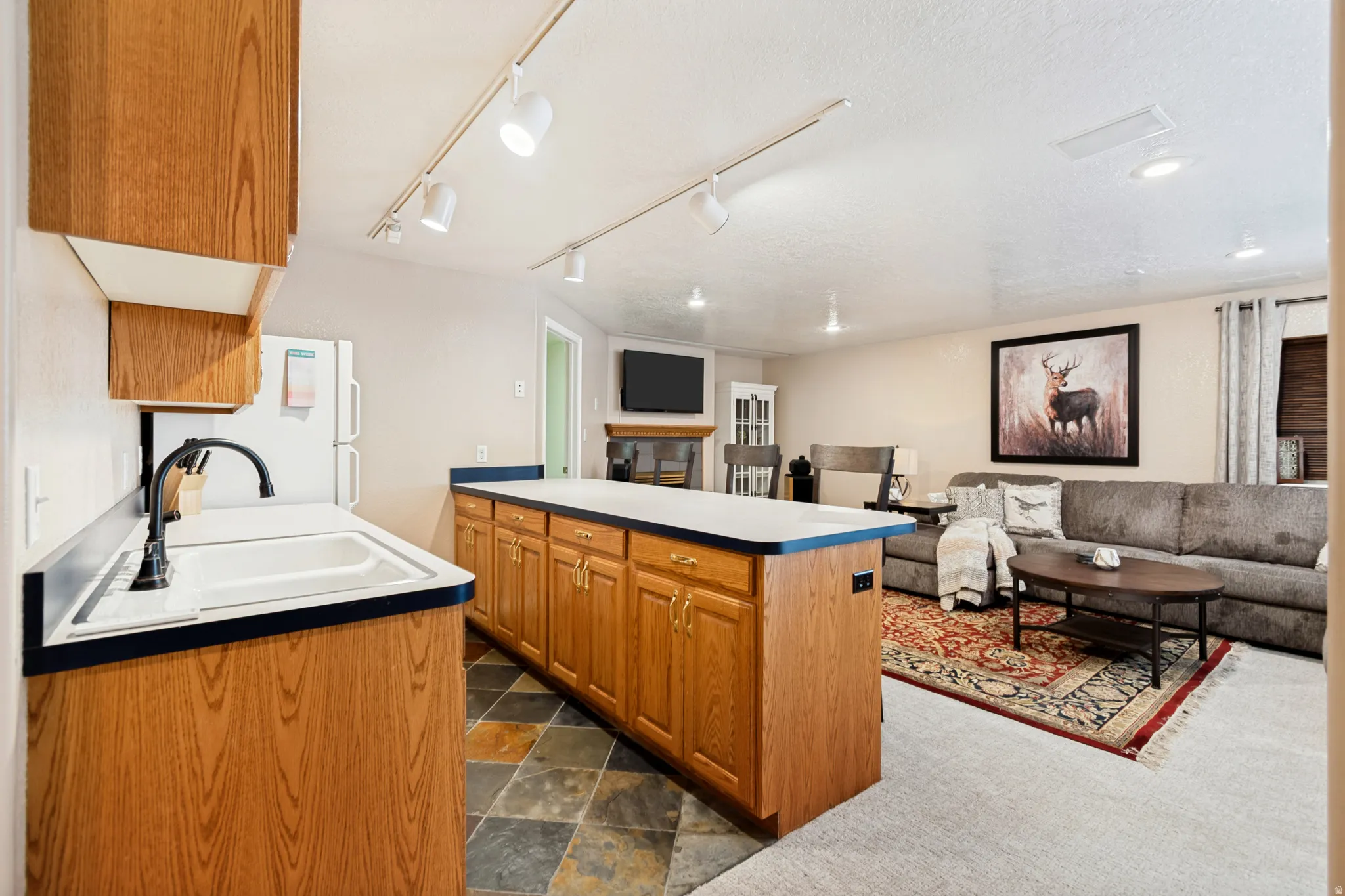Kitchenette featuring wood-finish cabinetry, white composite sink with matte black faucet, and slate-look tile flooring