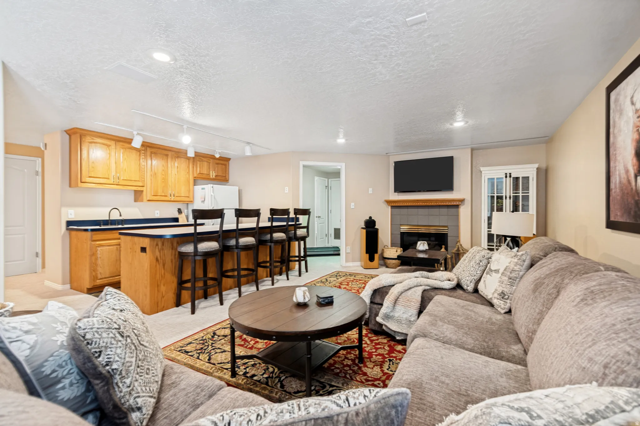 Combined living area featuring a built-in wet bar with wood cabinetry and countertop seating, a fireplace with a tile surround and wood mantel, recessed lighting, and a neutral wall color