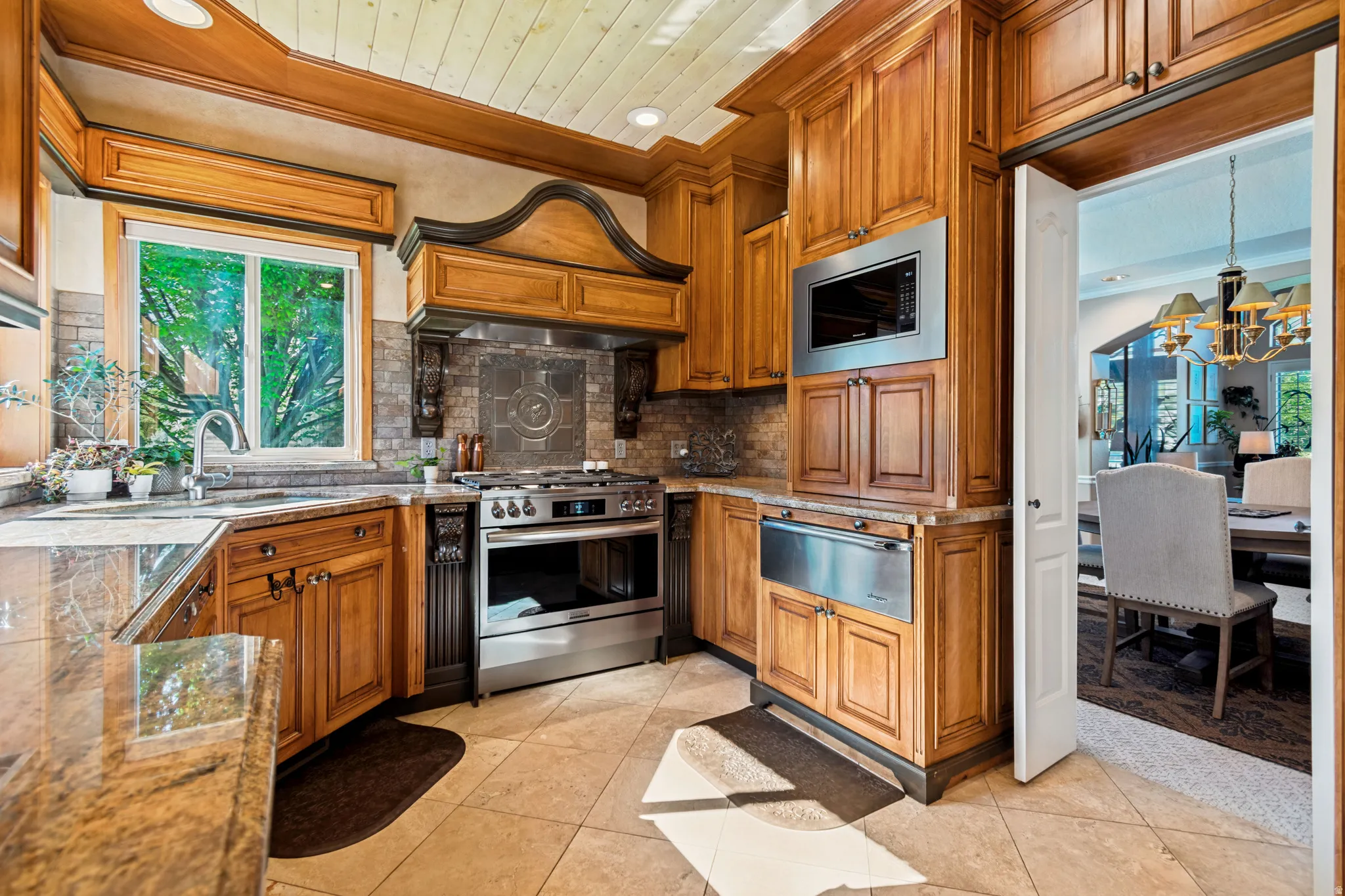 Gourmet kitchen featuring extensive wood cabinetry, stainless steel appliances, granite countertops, tile flooring, and a decorative range hood